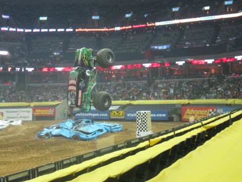 1994 Ford Bronco - Monster truck performing a stunt over crushed cars in a stadium, with a large crowd watching.