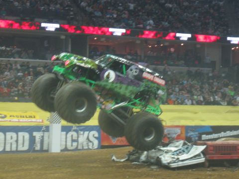 1994 Ford Bronco - A monster truck soars through the air, crushing cars below during an event.