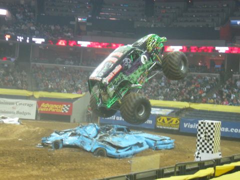 1994 Ford Bronco - A monster truck soars through the air over a pile of mangled cars during a competition.