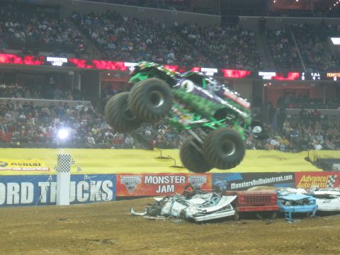 1994 Ford Bronco - The Grave Digger monster truck, painted purple and green with a graphic body, is captured mid-air jumping over a row of crushed junk cars a…