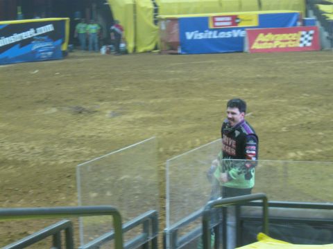 1994 Ford Bronco - A man in a racing shirt stands in an arena with dirt ground and banners in the background.