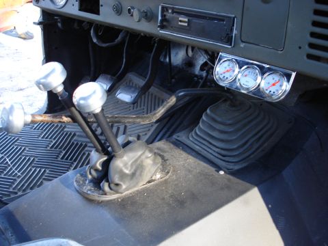 1971 Ford Bronco - The interior of a vehicle shows multiple shifters and aftermarket gauges on the dashboard.