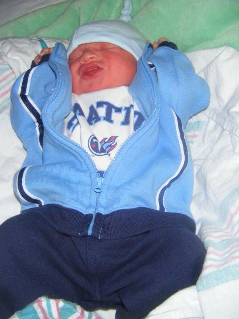1994 Ford Crown Victoria - A newborn baby is dressed in a blue outfit, lying down with eyes closed.