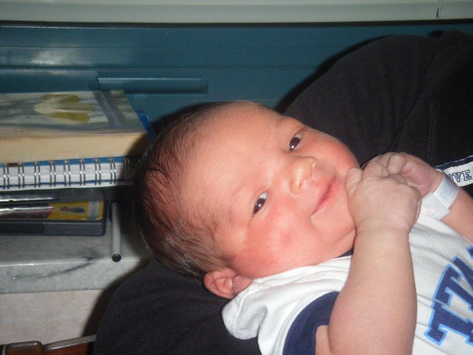 Newborn baby with hospital wristband resting on an adult's arm, notebooks in background