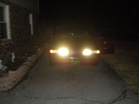 1994 Ford Crown Victoria - A red sedan is parked in a driveway at night, its headlights illuminating the scene.