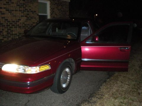 1994 Ford Crown Victoria - A red sedan is parked outside a brick building at night with its driver's door ajar.