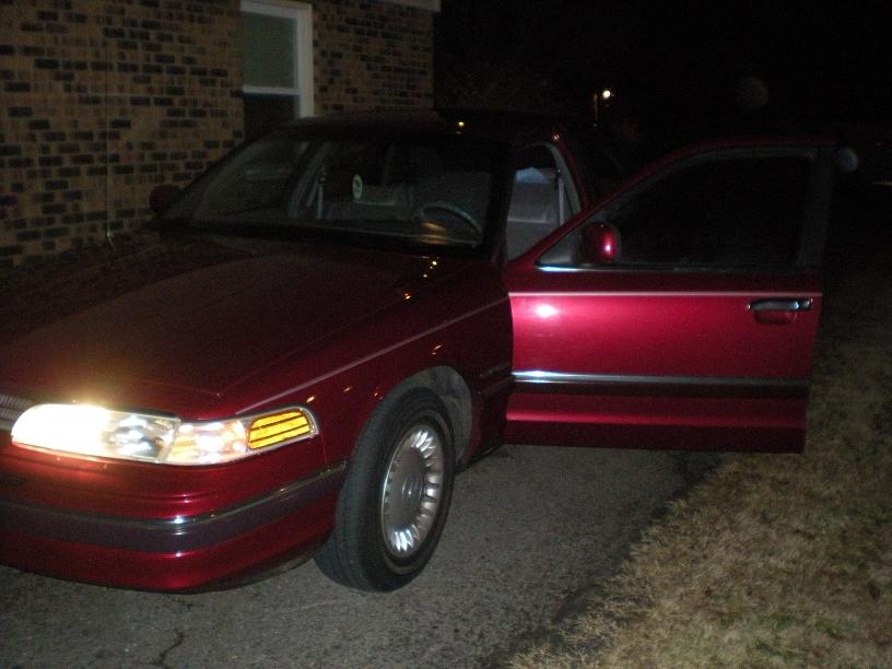 Red sedan with driver's door open, front quarter view, headlights on