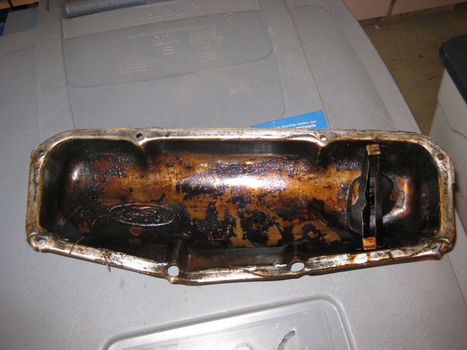 Ford oil pan with visible Ford logo, covered in old oil and grime