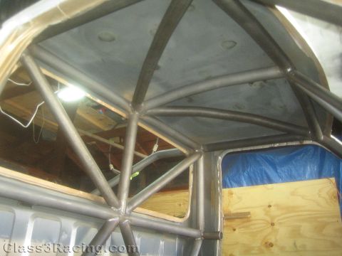 1990 Ford Bronco - Looking up at the roof interior of a stripped vehicle showing intersecting bare-metal roll cage tubing and welded joints.