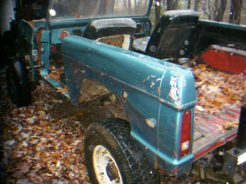1978 Ford Bronco - A teal 1978 Ford Bronco shows significant wear and tear, with its interior exposed and the bed filled with leaves.