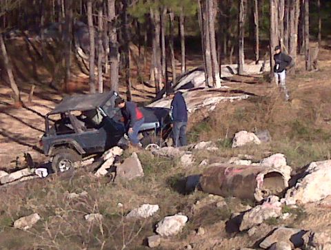 2008 Jeep Wrangler - A dark colored Jeep Wrangler is parked on a rocky incline, with people gathered around it in a wooded area.
