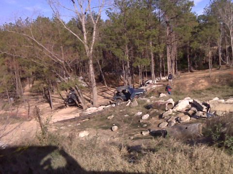 2008 Jeep Wrangler - Two off-road vehicles are parked on a dirt hill surrounded by trees and rocks.