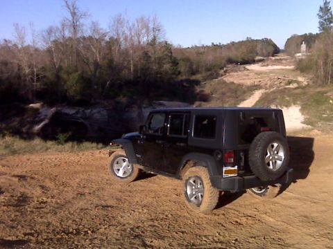 2008 Jeep Wrangler - A black Jeep Wrangler navigates a dirt path in a wooded, hilly area.