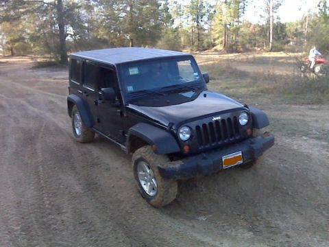 2008 Jeep Wrangler - A black 2008 Jeep Wrangler navigates a dirt path, with a wooded area and a person on an ATV visible in the distance.