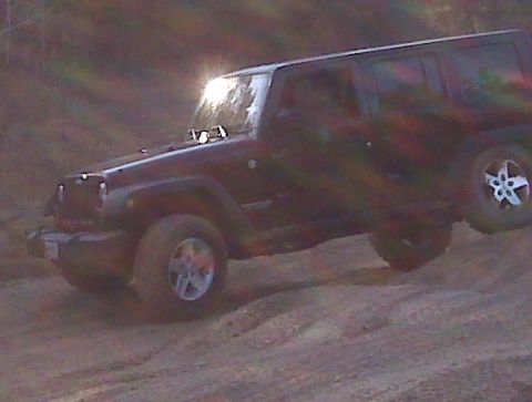 2008 Jeep Wrangler - A Jeep Wrangler navigates a dusty, off-road trail with its headlights illuminated.