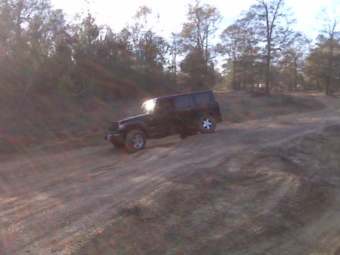 2008 Jeep Wrangler - A black Jeep Wrangler navigates a dirt incline with its front-right wheel lifted.