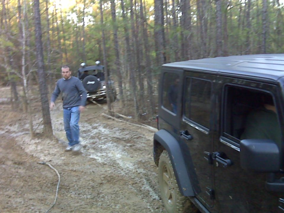 Black Jeep Wrangler on muddy trail with another Jeep behind it