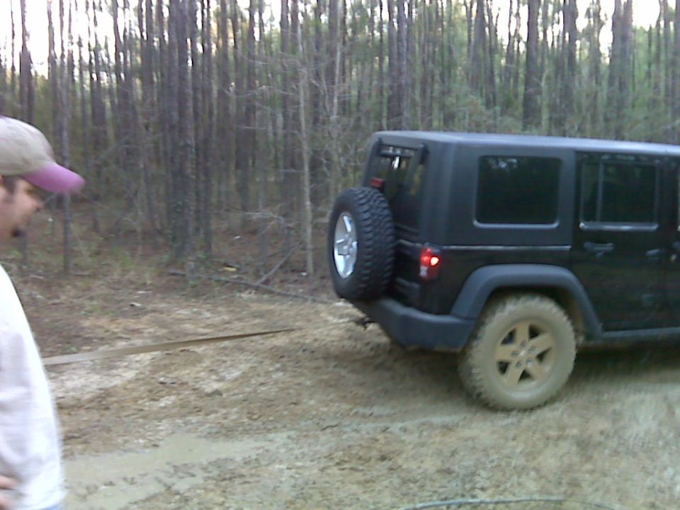 Black 2008 Jeep Wrangler parked on a muddy dirt road with trees in the background