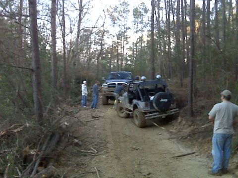 2008 Jeep Wrangler - Two off-road vehicles are stopped on a dirt path surrounded by trees, with several people observing.
