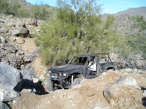 1986 Toyota Hilux - A modified black pickup truck navigates a challenging rocky terrain in a desert landscape.