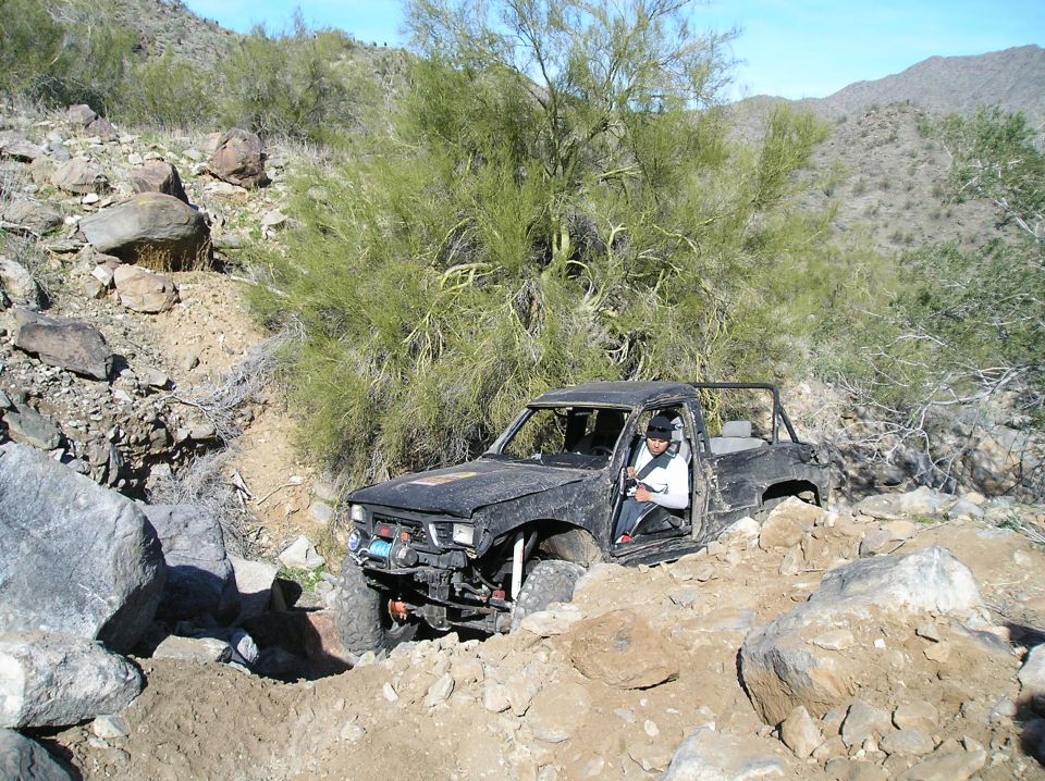 Black pickup truck with roll cage, off-roading in a rocky, desert environment