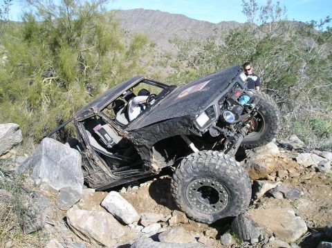 1986 Toyota Hilux - A heavily modified off-road vehicle attempts to climb over large rocks on a dry, mountainous landscape.