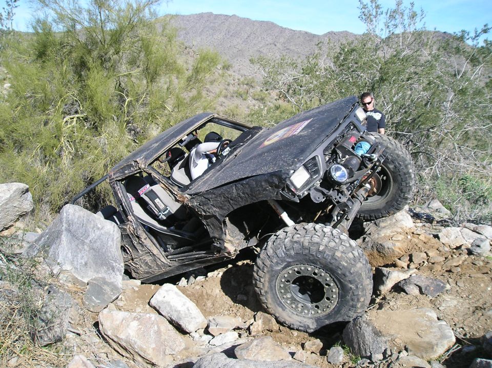 Off-road vehicle with large tires navigating a rocky trail, driver visible