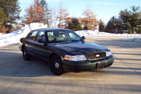 2001 Ford Crown Victoria - Dark green sedan with police equipment parked outside in winter conditions.