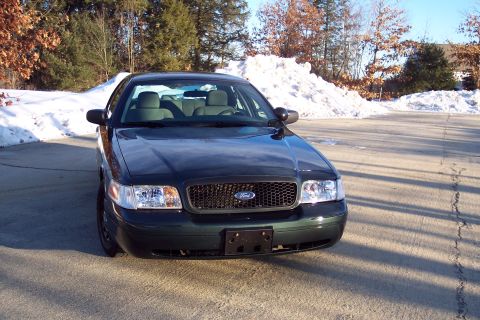 2001 Ford Crown Victoria - A dark green Ford Crown Victoria is parked on a paved surface with snow in the background.