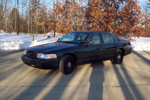 2001 Ford Crown Victoria - A dark green 2001 Ford Crown Victoria sedan is parked on a paved surface with snow and trees in the background.