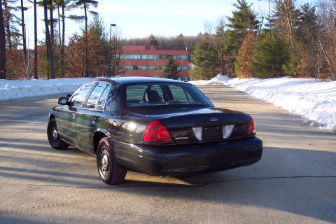 2001 Ford Crown Victoria - A dark sedan is parked on a road with snow lining the sides, viewed from the rear.