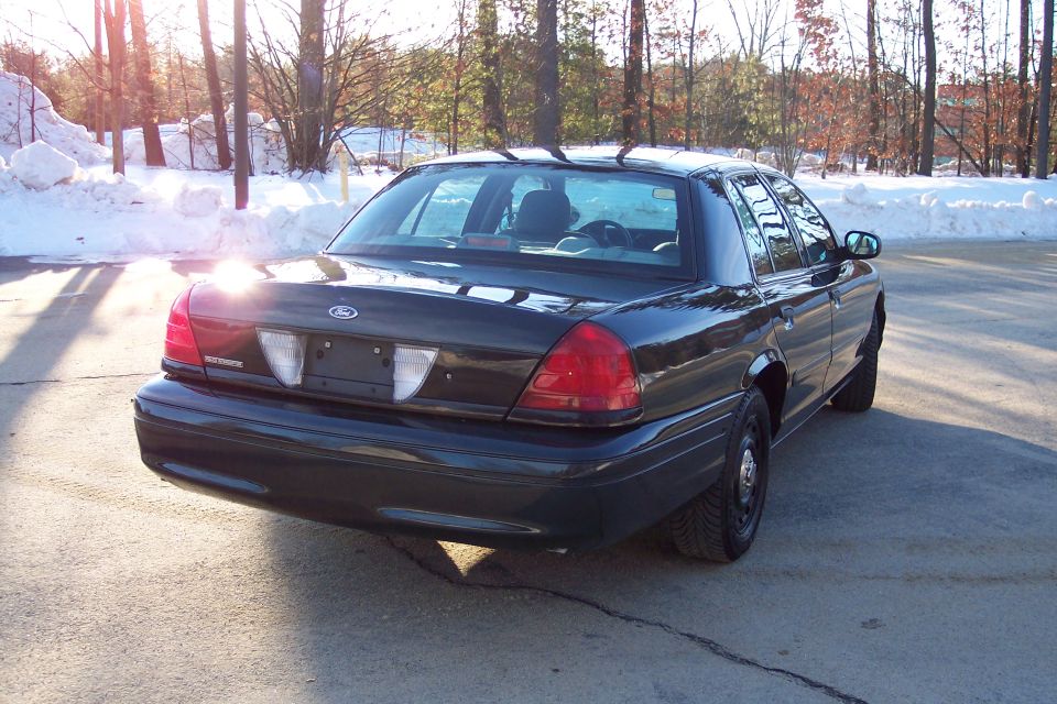 Dark Ford Crown Victoria parked on asphalt with snow in background