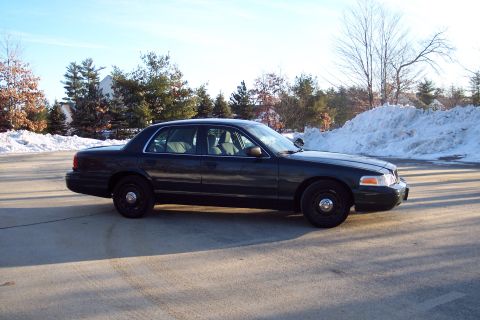 2001 Ford Crown Victoria - A dark-colored sedan is parked on a paved surface with snowbanks visible in the background.