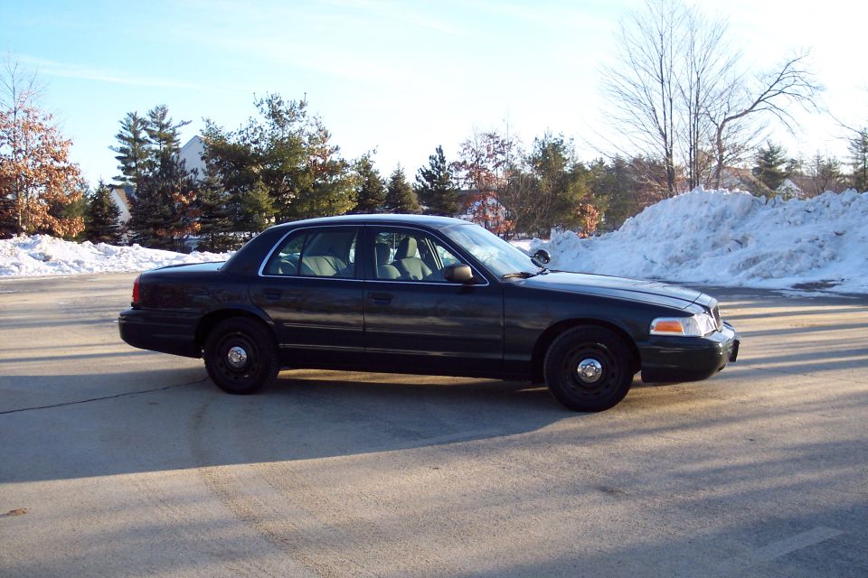 Dark sedan parked on pavement with snow piles in background. Looks like a Ford Crown Victoria