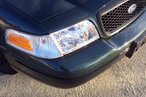 2001 Ford Crown Victoria - Close-up of the front corner of a dark green 2003 Ford Crown Victoria, showing the headlight and grille details.