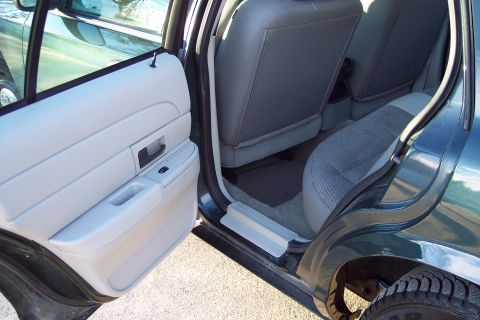 2001 Ford Crown Victoria - The interior of a dark green sedan is shown, with the front passenger door open, revealing the door panel and rear seating area.