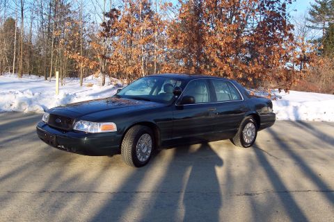2001 Ford Crown Victoria - A dark green Ford Crown Victoria is parked on a paved surface with snow and trees in the background.
