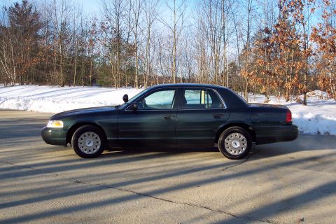 2001 Ford Crown Victoria - Side view of a dark green sedan with a police light on the driver's side roof.