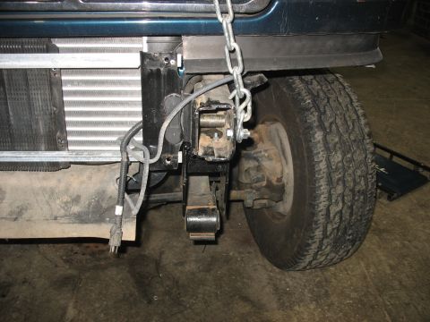 1995 Ford C-350 (Centurion Conversions) - Close-up view of the front suspension components and radiator of a vehicle, with a chain attached to the frame.