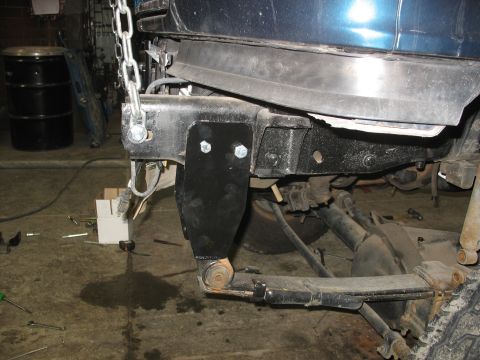 1995 Ford C-350 (Centurion Conversions) - Close-up view of a custom suspension bracket being installed on a blue truck's frame, showing leaf spring and axle components.