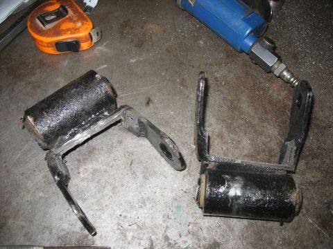 1995 Ford C-350 (Centurion Conversions) - Two black metal suspension parts with rubber bushings are shown on a metal surface next to a tape measure and air tool.