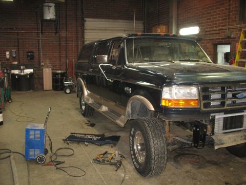 1995 Ford C-350 (Centurion Conversions) - A black Ford Bronco is parked in a garage, undergoing some mechanical work.