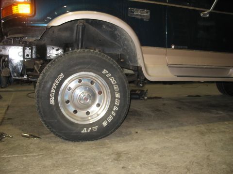 1995 Ford C-350 (Centurion Conversions) - The front wheel and side of a 1995 Ford C-350 (Centurion Conversions) van are visible, showing its two-tone paint scheme.