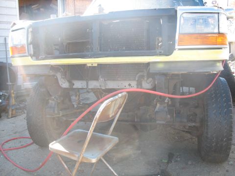 1987 Ford Bronco - Front view of a yellow Ford truck with its grille removed, revealing the radiator and front end damage.