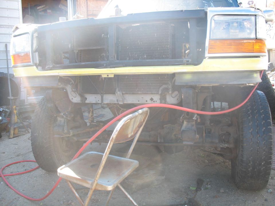 Yellow Ford truck front end with grille removed, showing radiator and bumper damage