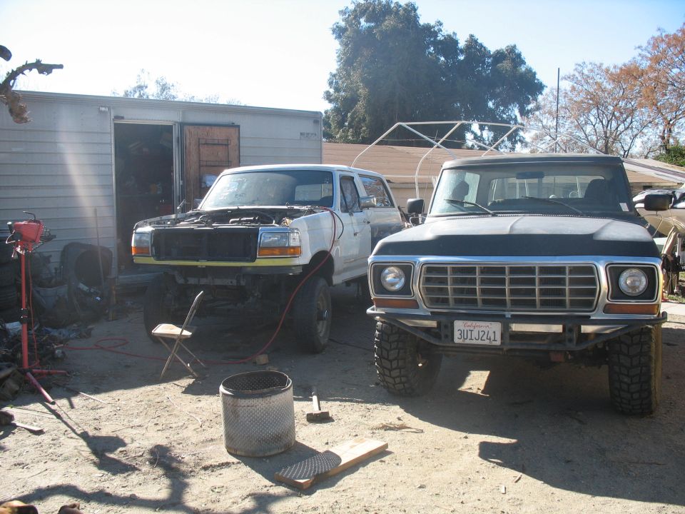 Front view of a dark 1970s Ford F-Series truck with a custom bumper and a white Ford Bronco in the background