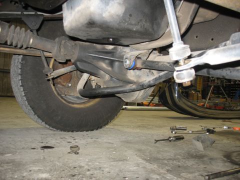 1995 Ford C-350 (Centurion Conversions) - Close-up of vehicle undercarriage components, including suspension and a tire, with tools nearby.