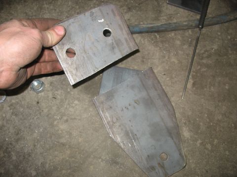 1995 Ford C-350 (Centurion Conversions) - Two metal bracket components, likely for a vehicle suspension system, are shown with a hand holding one piece.