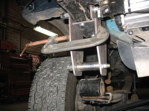 1995 Ford C-350 (Centurion Conversions) - Close-up of a custom suspension modification, showing a C-clamp securing a metal bracket near a tire.
