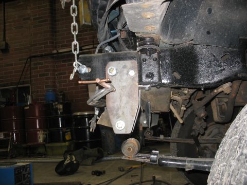 1995 Ford C-350 (Centurion Conversions) - A custom bracket is being installed on the vehicle's frame, with a chain hoist overhead.